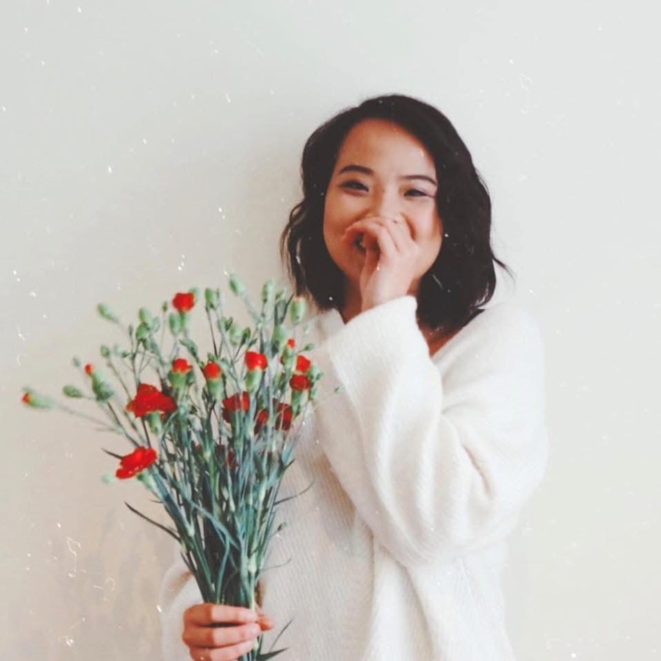 Nguyen Tra My laughing, holding a bunch of red carnations against a pale wall
