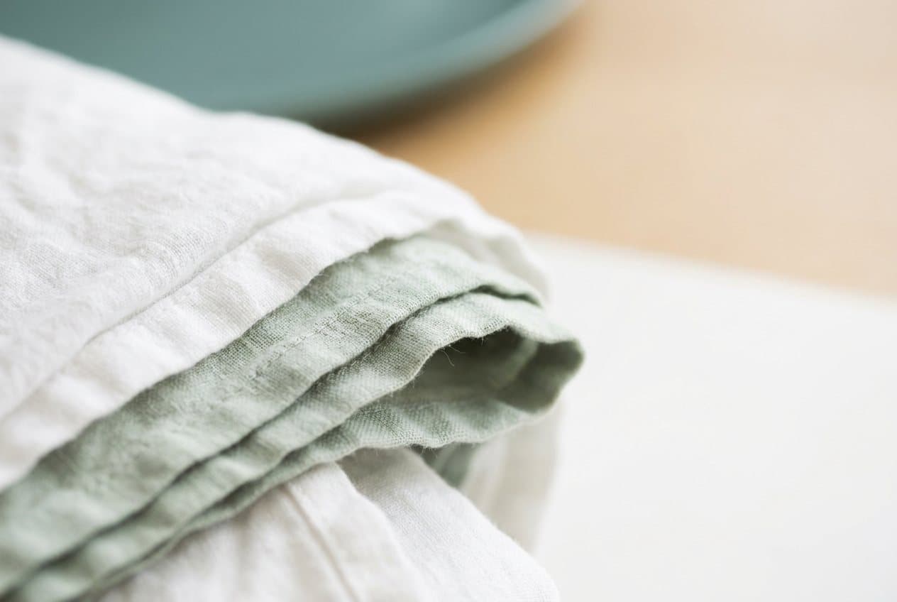 Close detail of the folded edges of white and pale sage cotton linen